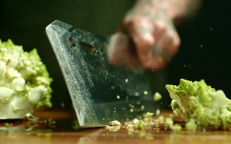 A person uses a cleaver to cleave a large vegetable in two on a wooden cutting board