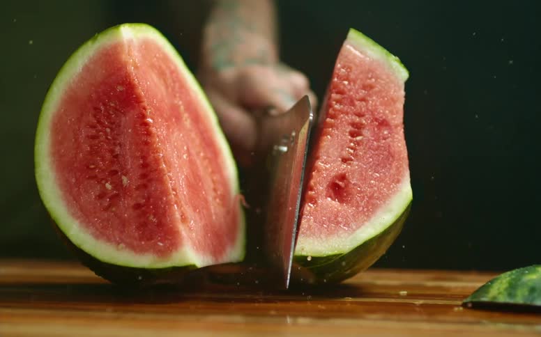 A person chopping a watermelon with a cleaver on a cutting board