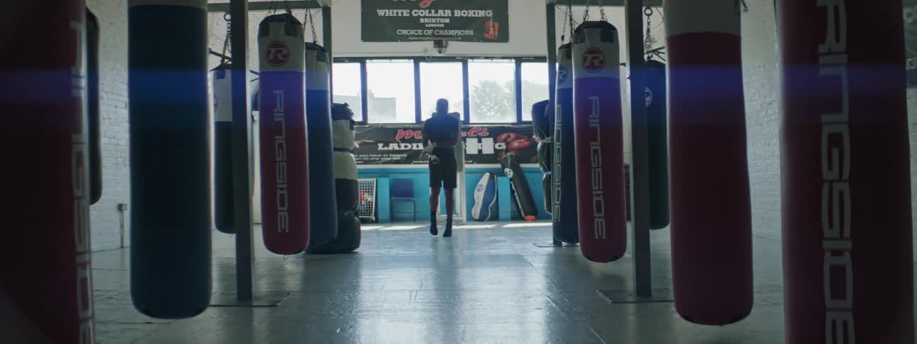 Young fit man jumping rope among punching bags in a gym at daytime