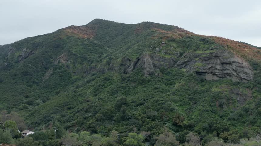 A house is visible at the base of a rocky and green mountain