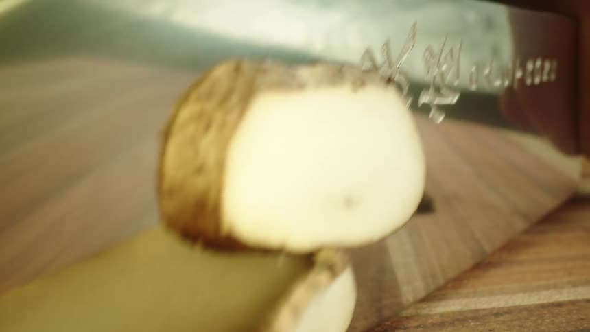 Close up of a tattoed man slicing mushrooms with a sharp kitchen knife over a wooden board
