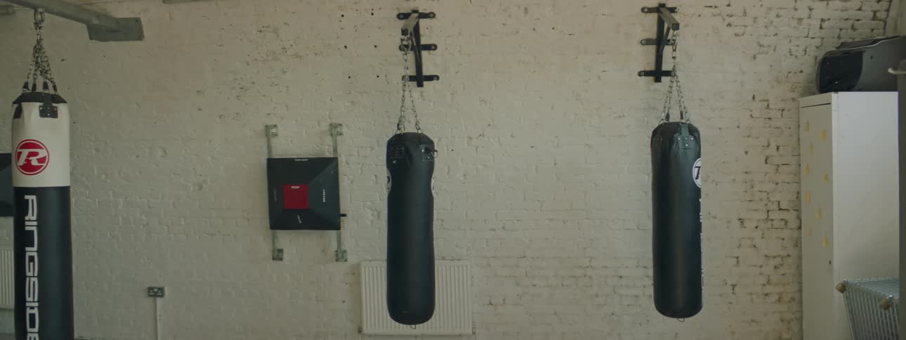 A boxing gym with heavy bags hanging over the floor with a wall in the background