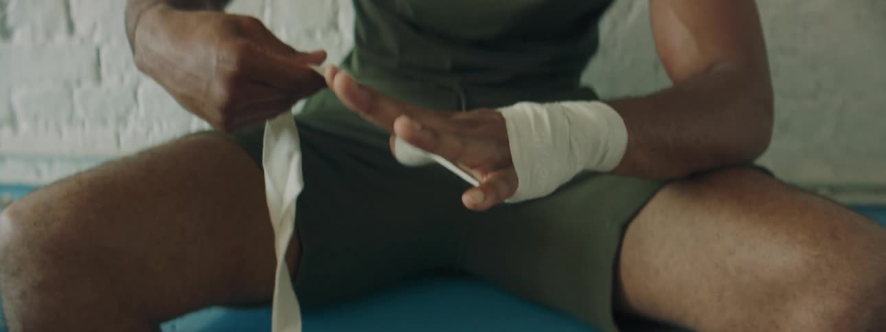 Boxer sitting in a bench wraps his fingers and hands with white bandages
