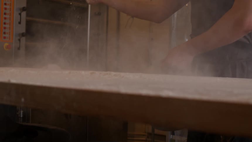 A man spreads flour unto a wood surface