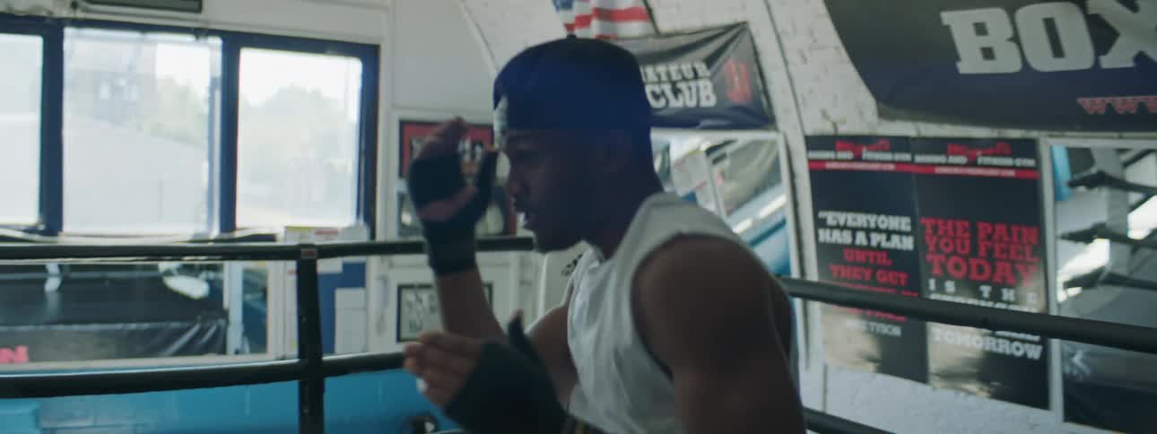 A man shadow boxes in a boxing ring in a gym during the day