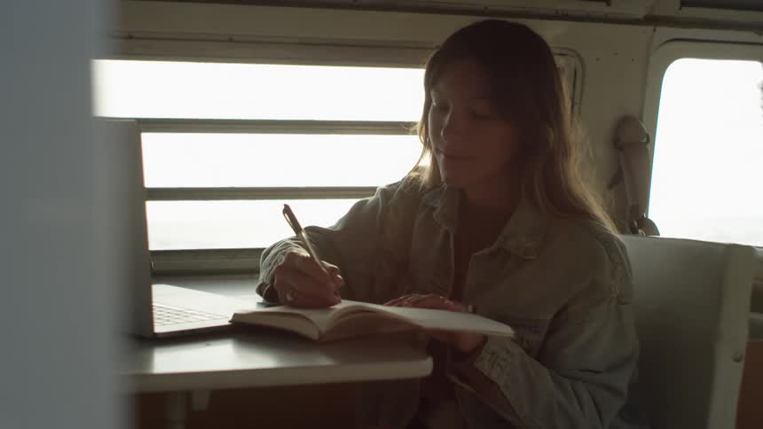 A woman sitting in a van writing in a notebook