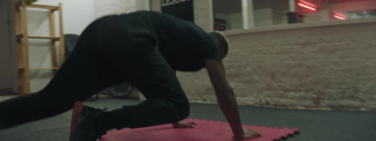 A man in a gym exercising on a mat with a wall and equipment in the background