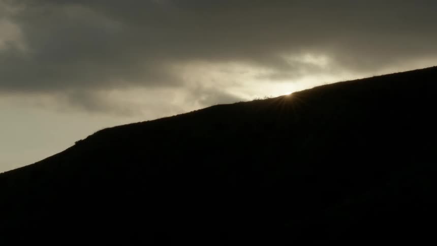 The sun sets and sinks below the silhouette of a hill