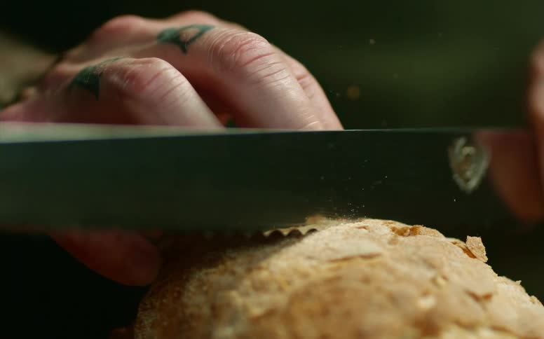 A person uses a bread knife to slice a flaky piece of bread