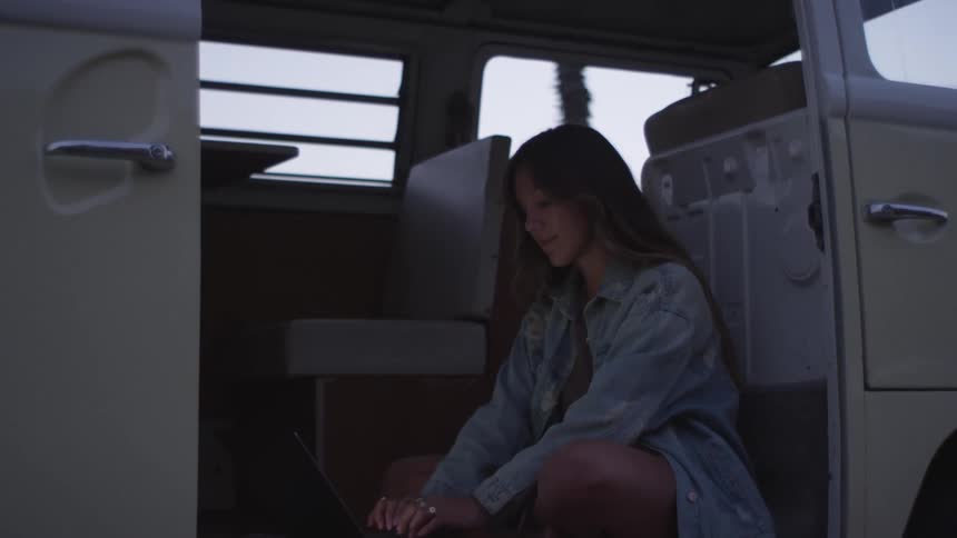 A woman is sitting in the van typing on her keyboard
