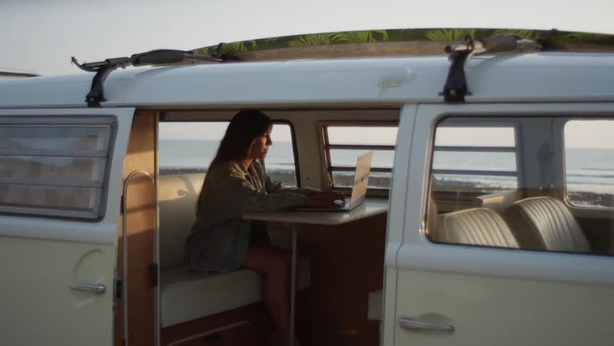 A woman sits in her van and types on a laptop