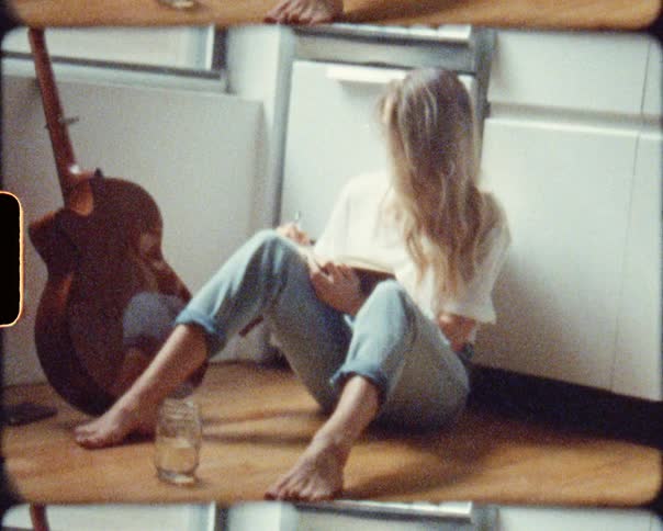 A woman sits on the floor next to her guitar while writing in her book