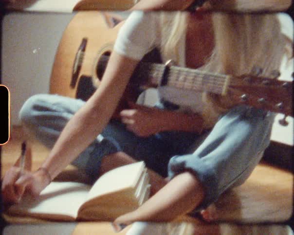 A woman is holding a guitar and writing in a journal