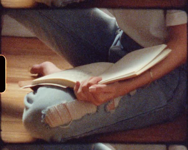 Blonde woman sits on wooden floor near guitar writing in notebook