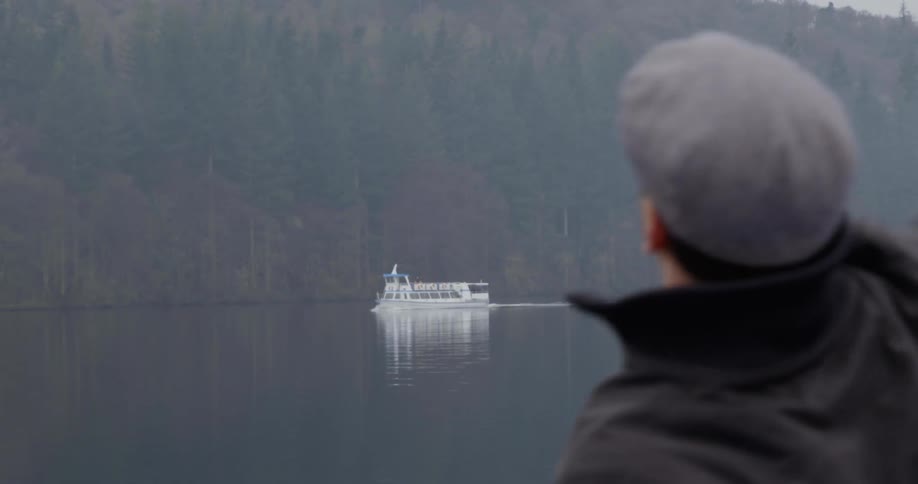 A man excitedly waves his arm at a ferry boat that is drifting past in the distance