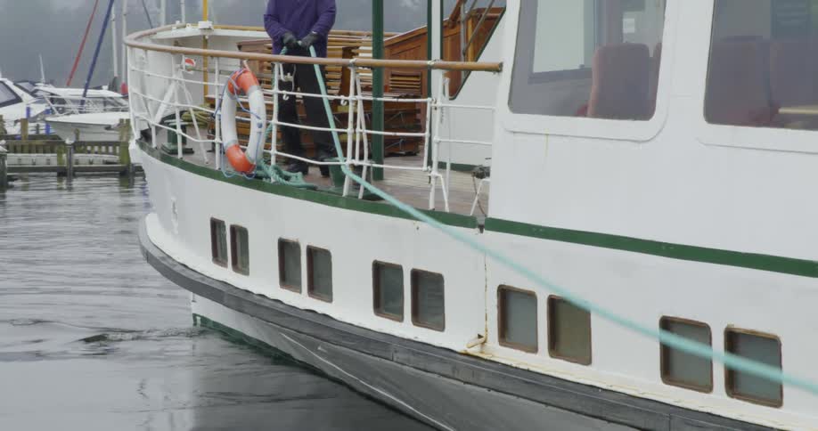 A sailor holds onto a rope while a ferry boat slowly turns