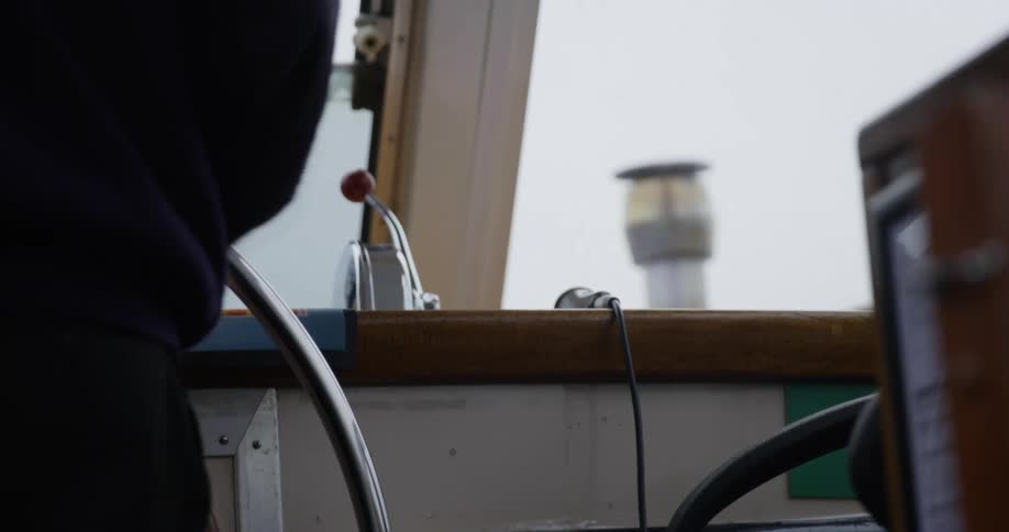 A person stands whiling spinning around the large steering while of a boat