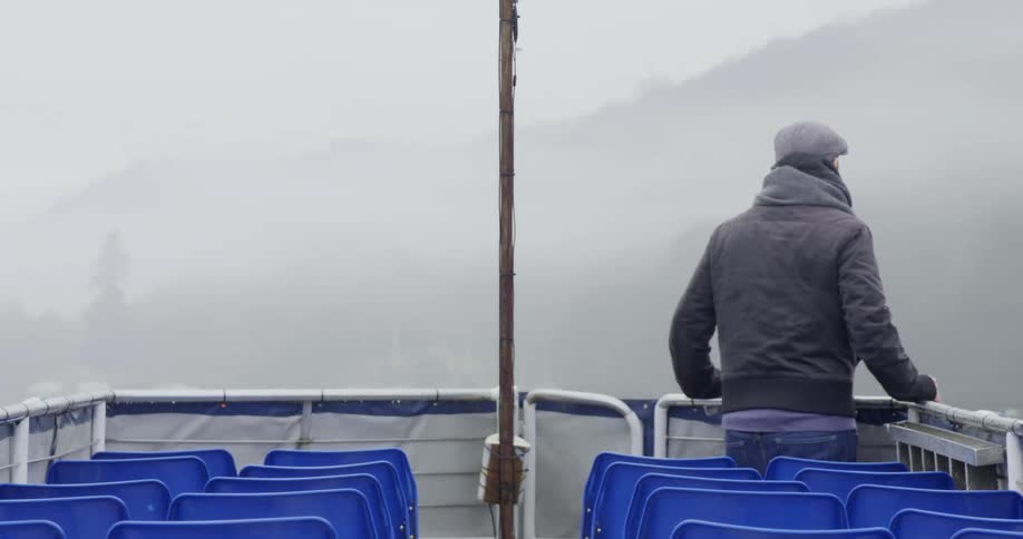 A man in a jacket riding on a boat on a foggy day