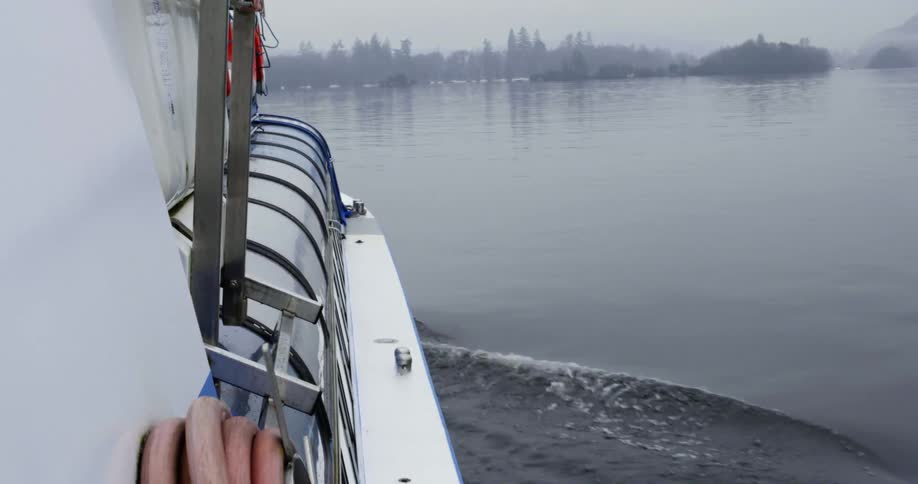 A ferry boat slowly motors across the water towards a forested shoreline on a foggy day