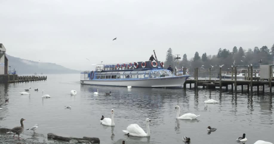 Small ferry boat docking in a pier in a lake near a mountain