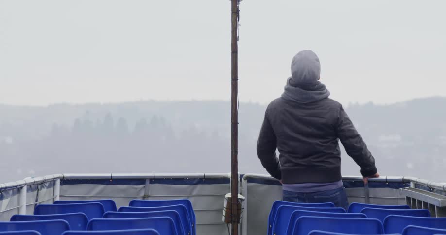 A man holds the ferry railing and leans back as he travels on a foggy day
