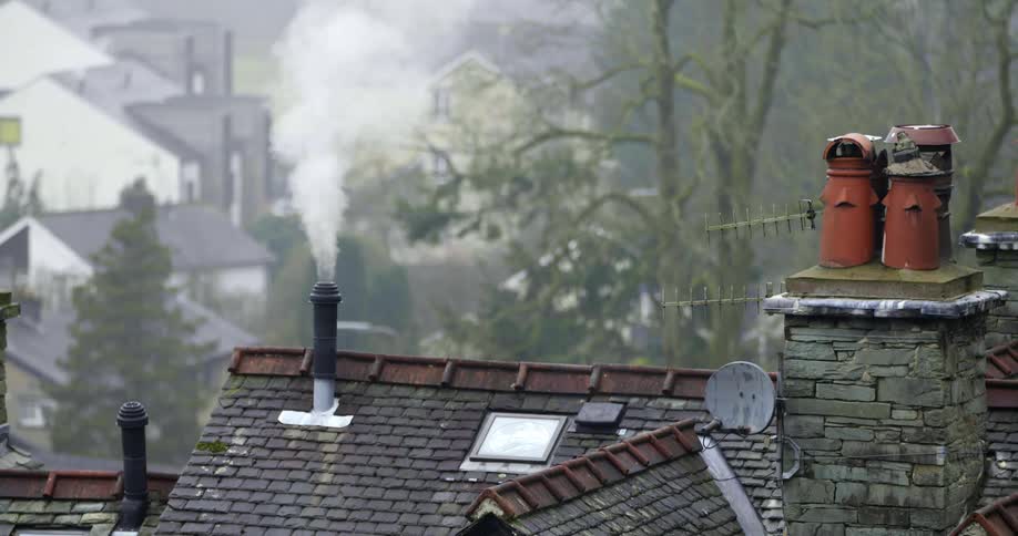 Rooftops with chimneys and antennas with trees and houses in the background