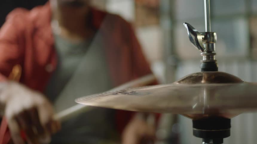 A drummer sitting at a drum set plays the drums using a pair of wooden drum sticks