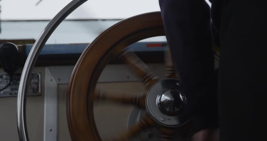 A person spins the steering wheel of a boat back and forth