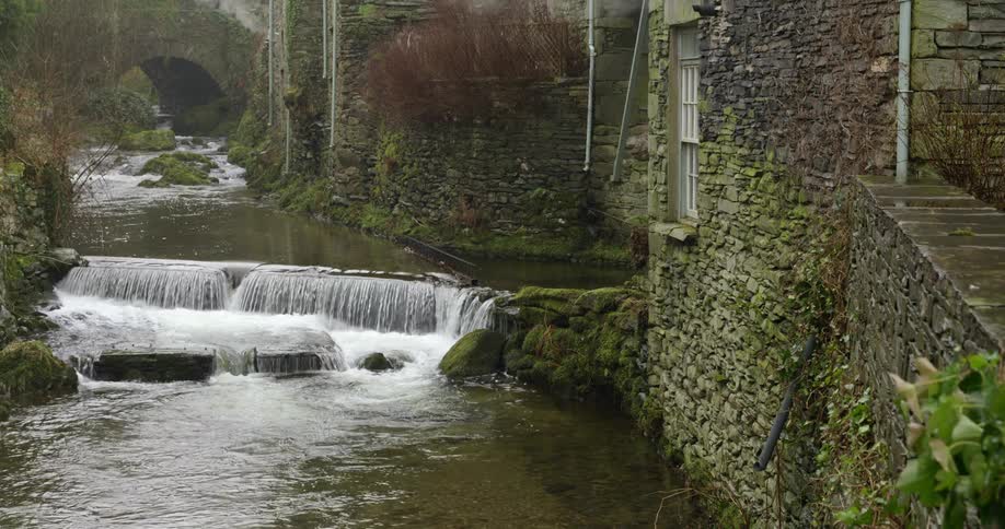 A river flowing by a mossy stone building in summer