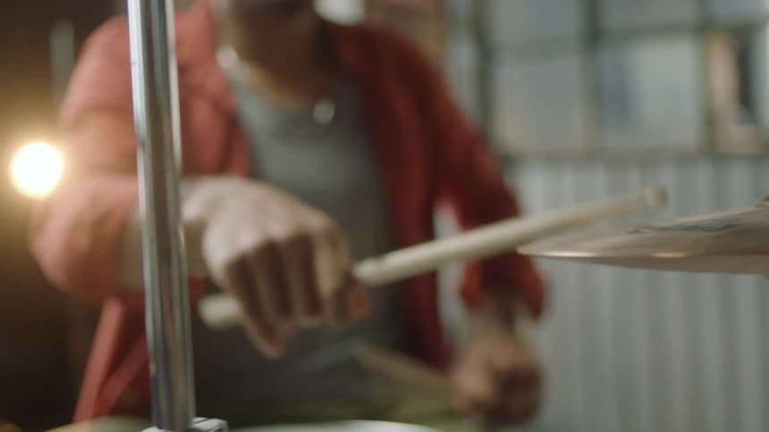 Person plays drums in room backed by yellow light bulb
