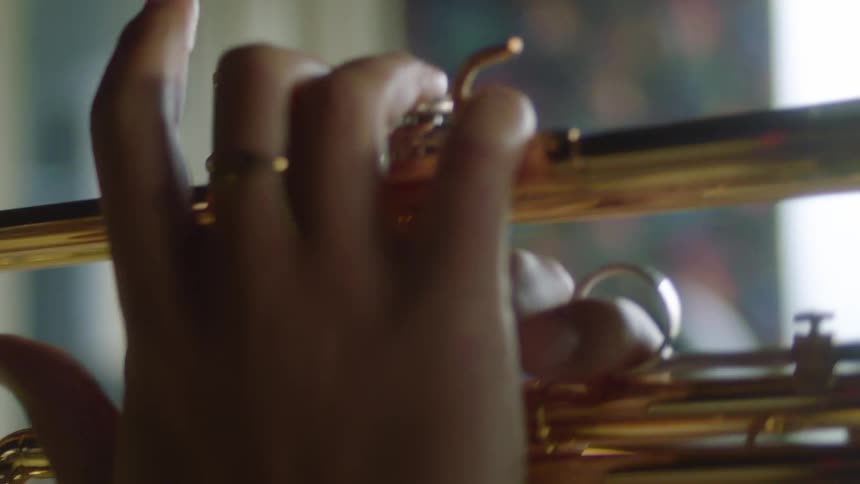 A person in a room with a ring playing the trumpet with a wall and a window in the background
