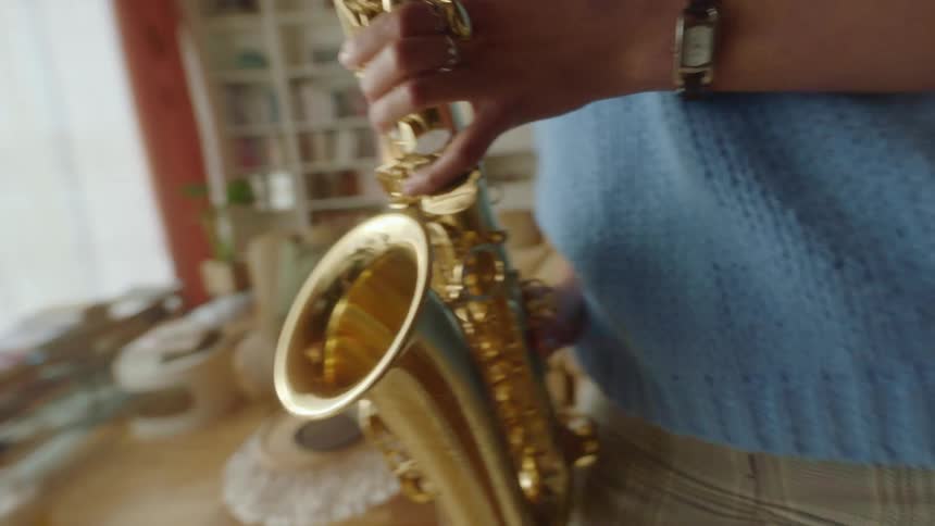 A saxophonist dances while playing the saxophone in the living room of a house during the day