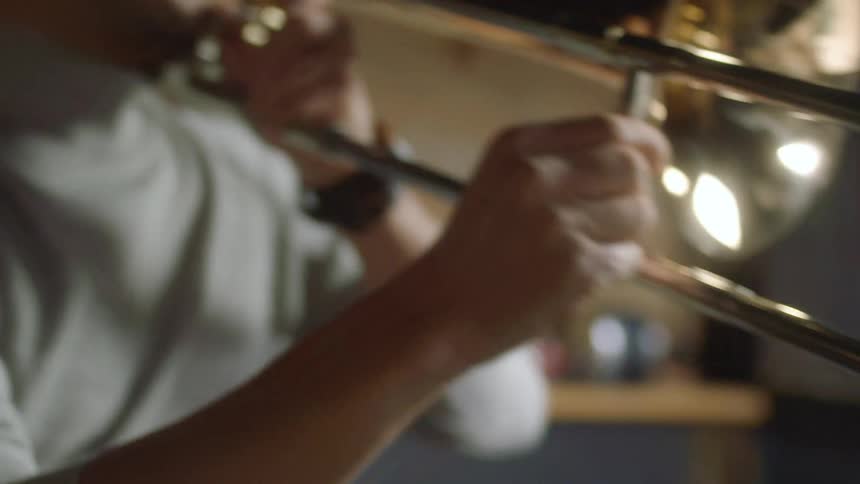 A person in a room with a wristwatch playing a trombone with a wall in the background