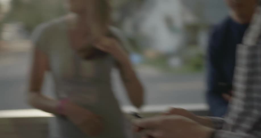 A man uses a phone as a woman laughs and talks with a group of people