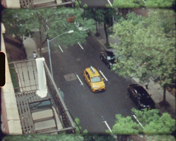 A taxi traveling on a city street lined by trees and buildings
