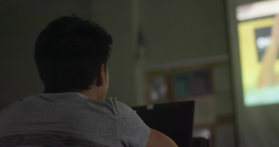 A man sitting in a room with a laptop in front of him and a projector on a screen