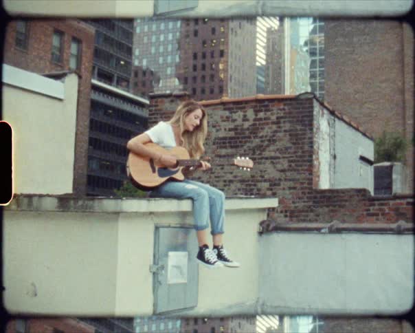A teenage girls sits below skyscrapers in a city and plays a guitar