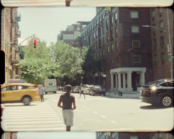A man waits to cross the street at a busy city intersection as traffic passes by