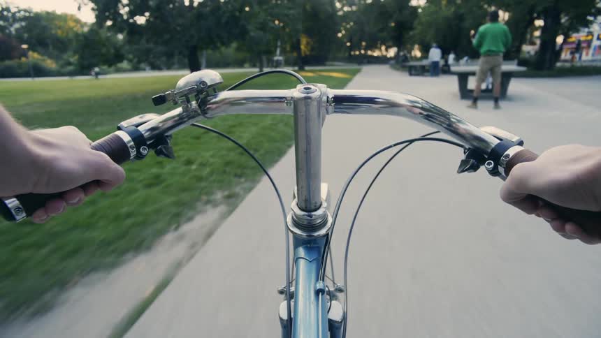POV: Person rides bicycle along path through park passing pedestrians and people playing ping pong
