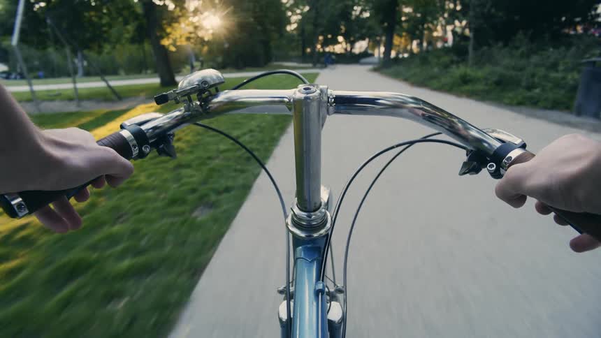 A bicyclist rides down a park trail and passes people playing ping pong POV