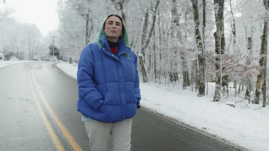 A teenage girl walks a long a road next to a snow covered forest