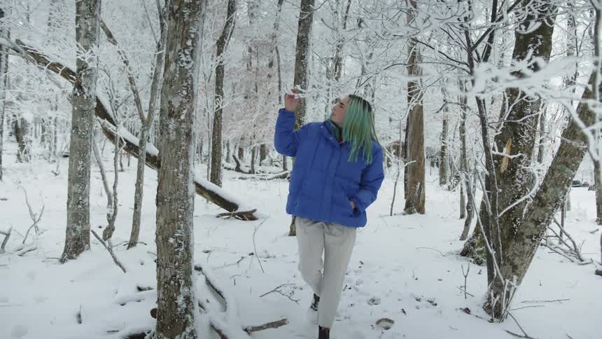 A woman touches a tree branch as she walks through a snow covered forest