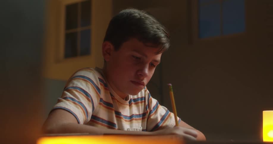A boy writes with a pencil as he does homework by a soft glowing light