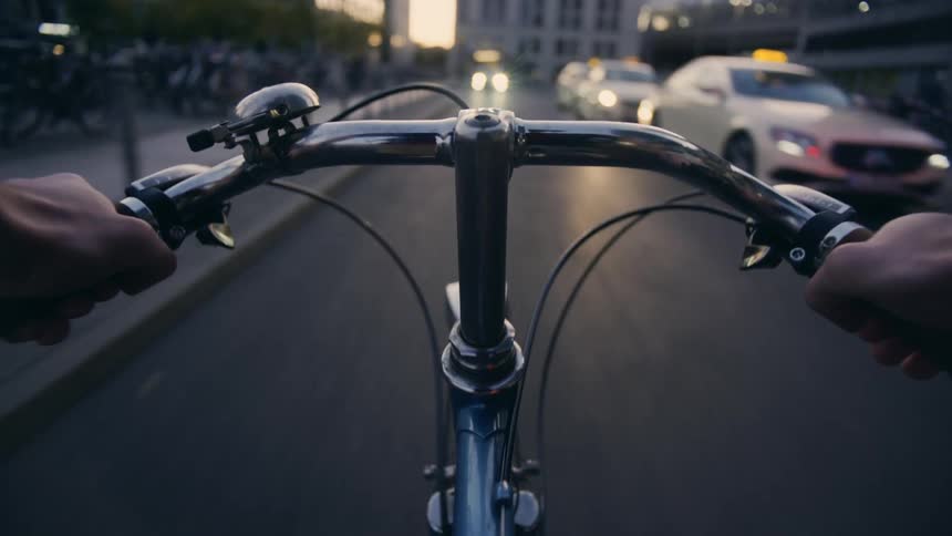 POV of a person cycles down a busy city street with cars driving and people walking