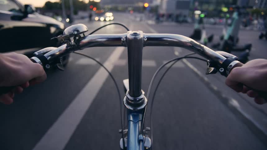 POV of a person cycling down a busy city street with cars and pedestrians