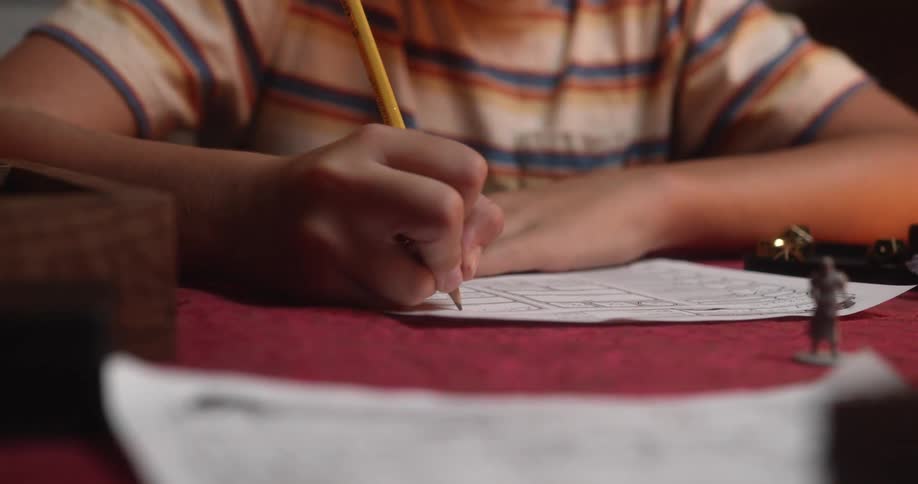 A child is writing on a a piece of paper while sitting indoors