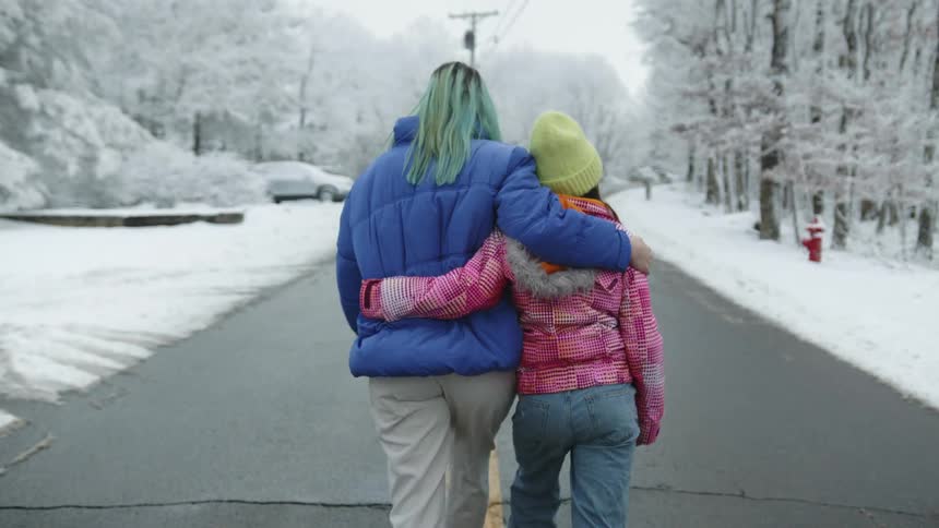 Woman and girl walk along cleared paved path through snow toward snow covered car and red fire hydrant