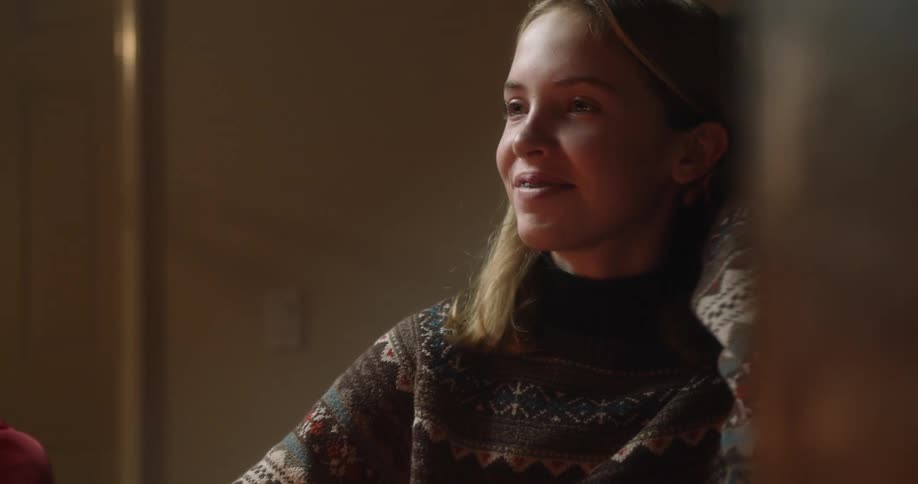 A girl in a room with a sweater smiling with braces with a wall and a door in the background