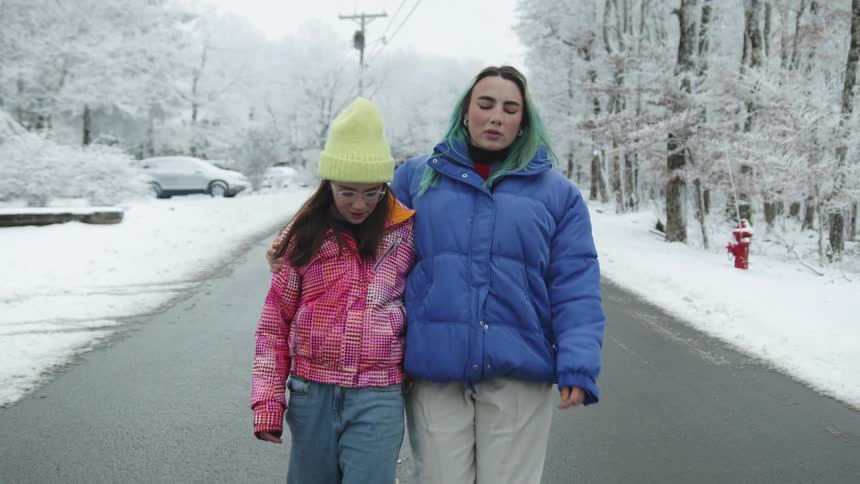A teenager walks down a neighborhood street with her arm around her younger sister