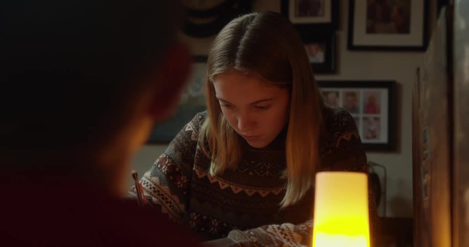 A girl in a room sitting at a desk writing with a pen next to a candle